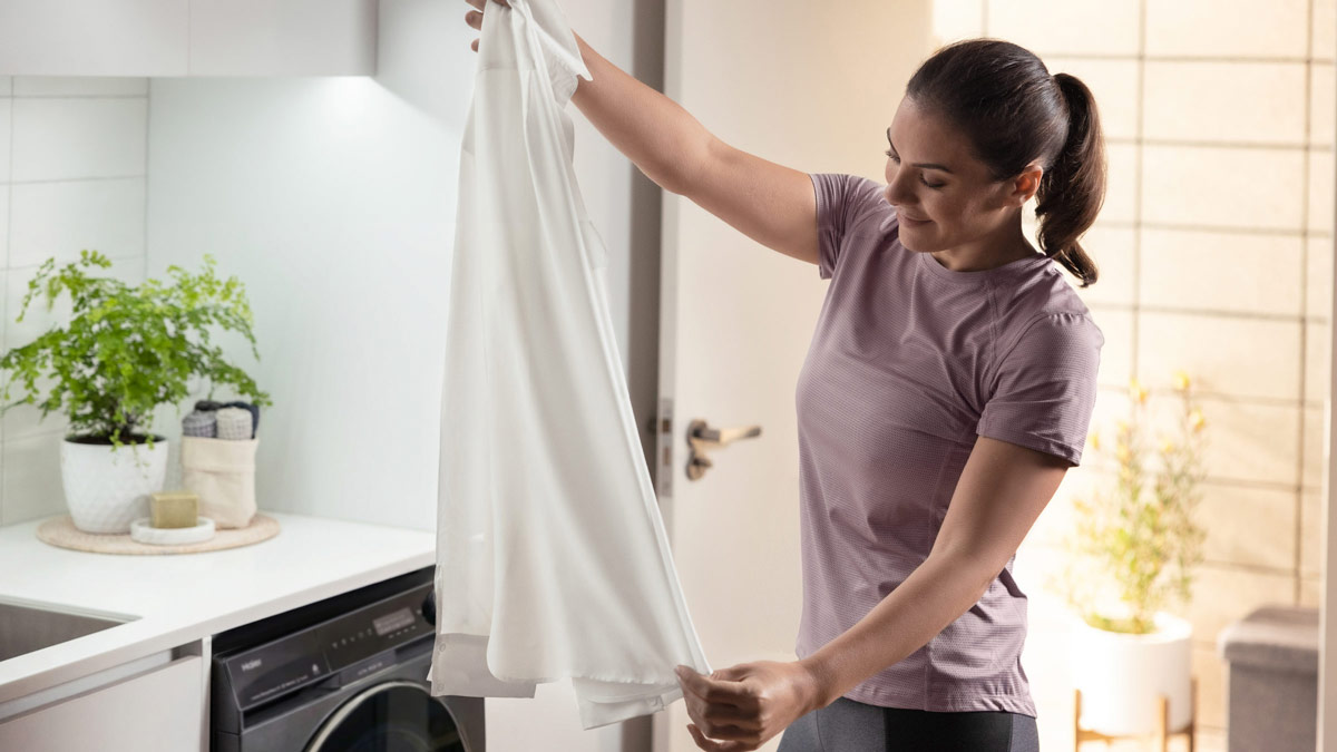 A woman holding a dress shirt in her laundry room